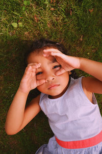 High angle view of a girl looking at camera and playing with her hands while resting on field