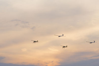 Low angle view of airplanes flying against sky during sunset