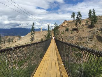 Footbridge amidst trees against sky