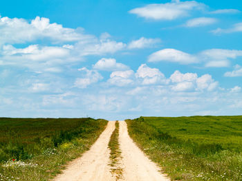 Dirt road amidst field against sky