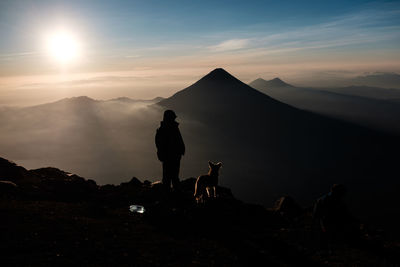 Silhouette people with dog on mountain range against sky