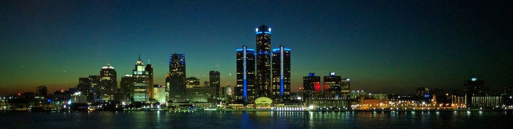 Panoramic view of illuminated modern buildings and river against sky in city at night