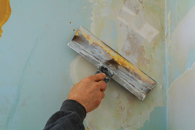 Close-up of cropped hand scraping paint on wall