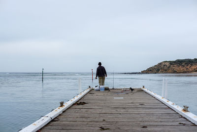 Rear view of man standing on pier over sea against sky