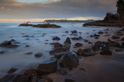 Rocks on beach against sky during sunset