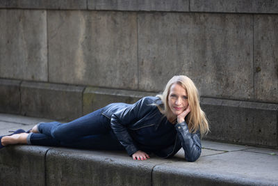 Portrait of young woman sitting against wall