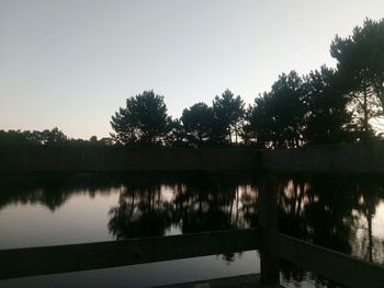 Silhouette trees by lake against clear sky