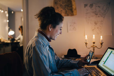 Smiling female engineer video conferencing on mobile phone while using laptop at desk