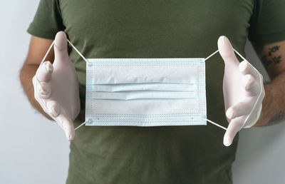 Midsection of woman holding paper while standing against white wall