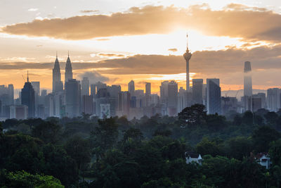 Trees and buildings against cloudy sky during sunset