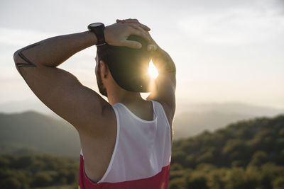 Sportsman with hands behind head admiring view while standing on mountain