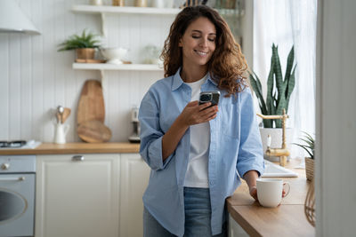 Portrait of smiling young woman using mobile phone while standing at home