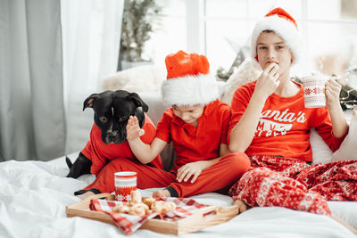 Cute kids drinking hot chocolate while sitting on bed with dog at home