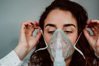 Close-up of woman wearing oxygen mask against gray background