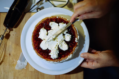 Person prepairing cake with whipped cream on table