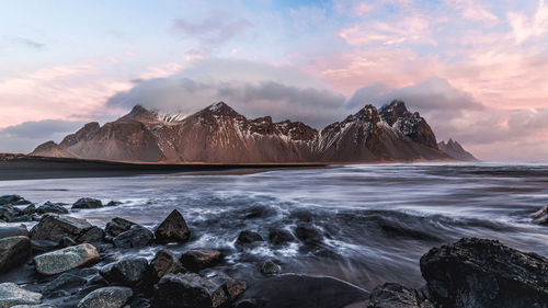 Scenic view of sea by mountains against sky during sunset