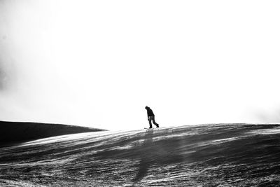 Silhouette man walking on snow covered shore against clear sky