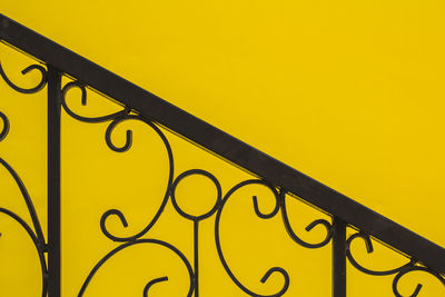 Low angle view of metal railing against yellow background