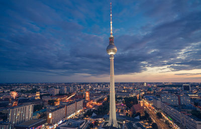 Aerial view of illuminated buildings in city against cloudy sky