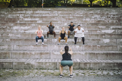 Rear view of female instructor teaching squats to team on steps at park