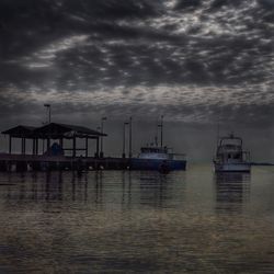 Boats in harbor against cloudy sky