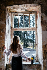 Rear view of woman standing by window at home
