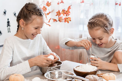 Two cute girls put eggs and flour into gingerbread dough for baking halloween cookies 