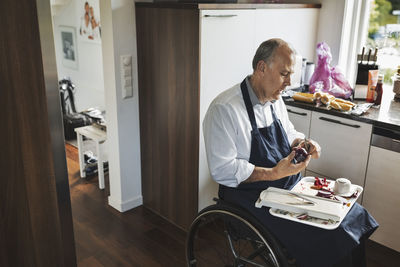 Disabled man in wheelchair cutting onion at kitchen