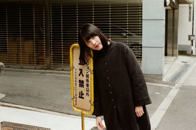 Woman leaning against a sign