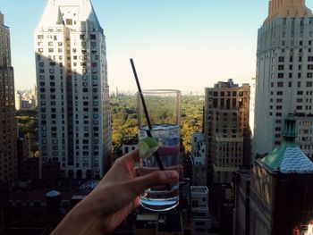 Cropped image of person holding lemonade in city against clear sky