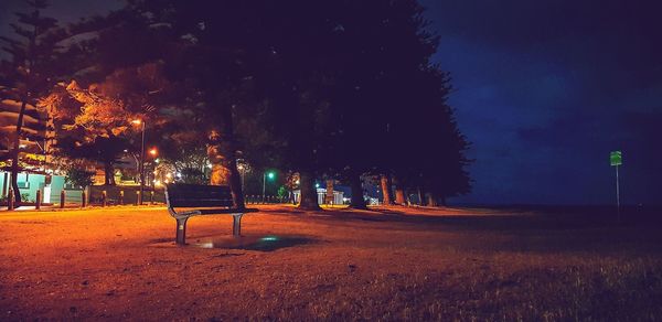 Empty bench on field against sky at night