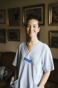 Smiling female caregiver with hands in pockets at nursing home