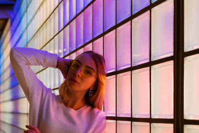 Portrait of young woman against illuminated wall