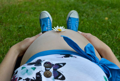 Low section of pregnant woman lying down with flower on belly in park