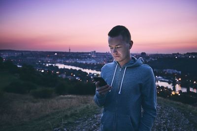 Mid adult man using mobile phone while standing against sky during sunset