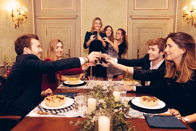 Group of positive friends looking at each other and toasting with wineglasses at table with tasty food during dinner in restaurant