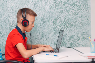 Side view of boy using mobile phone while sitting on table