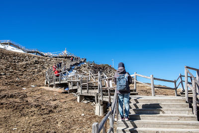 Rear view of people standing on staircase against clear blue sky