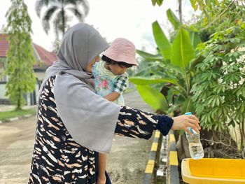 Rear view of man holding woman standing against plants