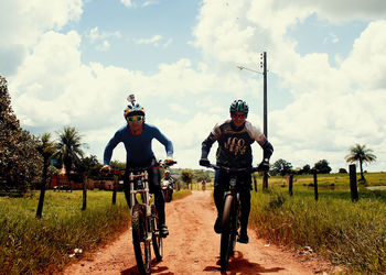 People riding bicycle on field against sky