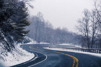 Road amidst trees against clear sky during winter