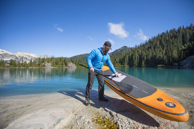 Adventurous man prepares to use sup on remote alpine lake.