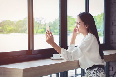 Side view of woman sitting on table at window