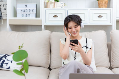 Young woman using phone while sitting on bed at home