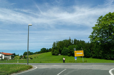 Empty road by trees against sky in city