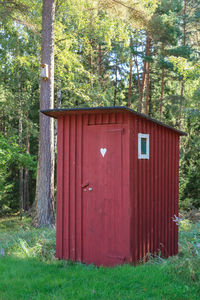 Red house on field by trees in forest