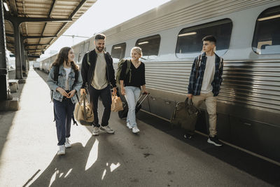 Father and mother walking with children carrying luggage near train at railroad station