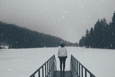 Rear view of man standing by railing during winter