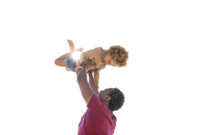 Cheerful father playing with daughter under clear sky on sunny day