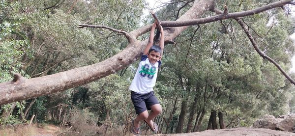 Full length of man climbing on tree trunk in forest